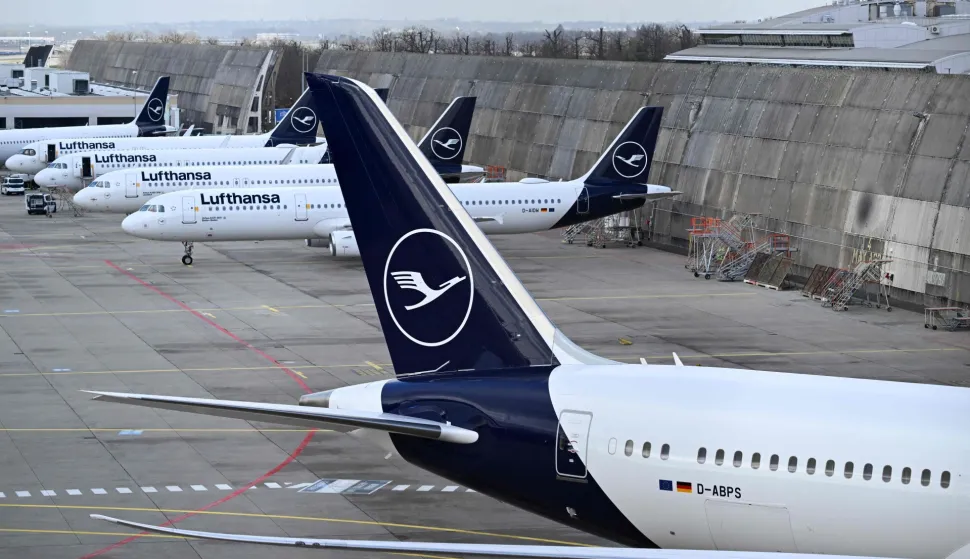 (FILES) The logo of German airline Lufthansa is seen on vertical stabilisers of aircraft parked on the tarmac while in the background an airplace is seen in flight at the international Frankfurt Airport, Frankfurt am Main, western Germany, on March 12, 2026. Cabin crew at German airline Lufthansa will go on strike on April 10, 2026 over an ongoing labour dispute, their union said. (Photo by Kirill KUDRYAVTSEV/AFP)