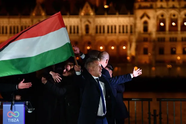 Peter Magyar, leader of the pro-European conservative TISZA party, waves the national flag on the banks on the river Danube with the Parliament building in the background, during their election night party in Budapest during the general election in Hungary, on April 12, 2026. Polls closed in Hungary's parliamentary election, with turnout reaching a record high in the crunch vote that sees nationalist Prime Minister Viktor Orban's 16-year stint in power face an unprecedented challenge from conservative political newcomer Peter Magyar. (Photo by Ferenc ISZA/AFP)