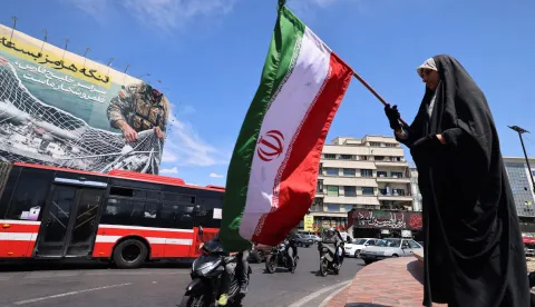 A woman waves Iran's national flag in front of a giant billboard reading 'The Strait of Hormuz remains closed' at the Revolution Square in Tehran on April 12, 2026. Iran's parliament speaker Mohammad Bagher Ghalibaf, who was part of peace talks with the United States this weekend, said on April 12 that Washington was "unable" to win Tehran's trust during the discussions. (Photo by ATTA KENARE/AFP)/