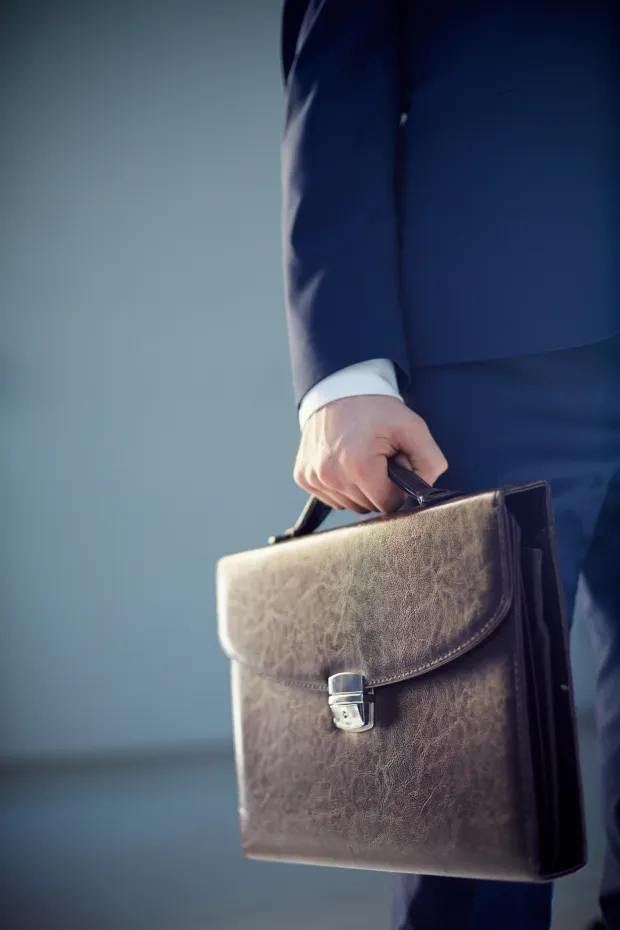 Vertical cropped image of a businessperson carrying a leather briefcase isolated on grey posao gospodarstvo ilustracija aktovka banka kredit pdv bdp gdp pregovori financiranje financije računovodstvo freepik