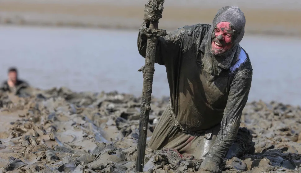 TOPSHOT - A participant wades through the mud as they compete in the annual Maldon Mud Race in Maldon, east England on April 26, 2026. Originated in 1973, the race involves competitors racing around a course through the River Blackwater in Essex at low tide. (Photo by Toby Shepheard/AFP)