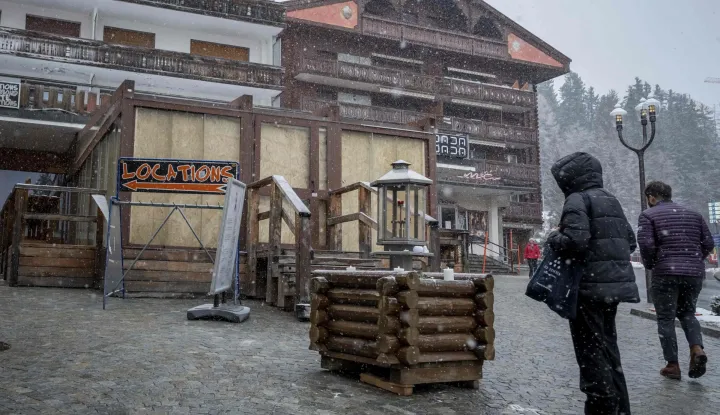 A pedestrian stands in front of the bar Le Constellation in the Alpine ski resort town of Crans-Montana on January 28, 2026, following the deadly fire that ripped through the bar on New Year's Eve celebrations. Public prosecutors in Switzerland's Wallis canton are facing a barrage of criticism over their handling of the investigation into the deadly New Year bar inferno. The January 1 blaze at Le Constellation in Crans-Montana left 40 people dead -- including nine French and six Italian nationals -- and injured 116 others. (Photo by Fabrice COFFRINI/AFP)