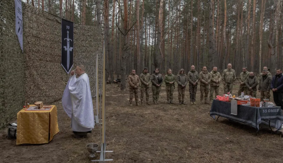 Military chaplain Mykola Bahirov prays with Ukrainian military members of the 33rd separate mechanised brigade next to traditional cakes and other food to celebrate Orthodox Easter, in the Kharkiv region, on April 12, 2026, amid the Russian invasion of Ukraine. A member of the Greek Catholic faith, this 39-year-old man was serving as a diocesan secretary when Russia launched its full-scale invasion of Ukraine in February 2022. It was at a soldier's funeral, when he saw the terror in the soldier's daughters, that Mykola Bahirov decided to become a chaplain: rather than accompany them in death, he would, while they were still alive, stay close to the Ukrainian soldiers fighting against the Russian invader. (Photo by Roman PILIPEY/AFP)