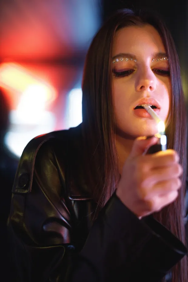 Fashion portrait of beautiful girl posing, dancing in colorful bright neon red lights. Model wearing trendy leather jacket and bright make up. Woman smoking sigarettes.cigarete pu&scaron;enje ilustracija