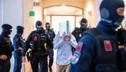 A 21-year-old defendant, who allegedly planned an attack on a Taylor Swift concert at the Ernst Happel Stadium in Vienna, hides behind a folder as Austrian justice guards guide him to the Regional Court of Wiener Neustadt, Lower Austria, on May 28, 2026. The court is expected to rule on May 28, 2026 in the trial of a 21-year-old man who has pleaded guilty to plotting a jihadist attack on a Taylor Swift concert. The three Vienna dates in the US megastar's record-breaking "Eras" tour were cancelled in the summer of 2024 after authorities warned of the plot. (Photo by Joe Klamar/AFP)