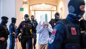 A 21-year-old defendant, who allegedly planned an attack on a Taylor Swift concert at the Ernst Happel Stadium in Vienna, hides behind a folder as Austrian justice guards guide him to the Regional Court of Wiener Neustadt, Lower Austria, on May 28, 2026. The court is expected to rule on May 28, 2026 in the trial of a 21-year-old man who has pleaded guilty to plotting a jihadist attack on a Taylor Swift concert. The three Vienna dates in the US megastar's record-breaking "Eras" tour were cancelled in the summer of 2024 after authorities warned of the plot. (Photo by Joe Klamar/AFP)