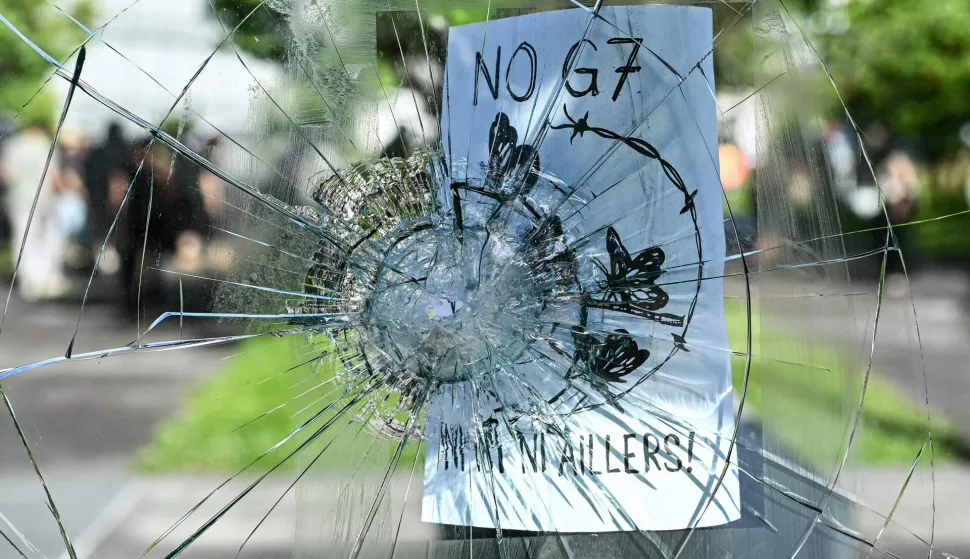TOPSHOT - This photograph shows a broken glass with a flyer reading "No G7, not here, not elsewhere" during a rally of a "No-G7" coalition of over 60 associations, unions and left-wing groups "against fascism and imperialism?, a day ahead of the summit's start, in Geneva on June 14, 2026. The 2026 edition of the G7 summit is set to take place June 15 to 17 in the French town of Evian-les-Bains near Switzerland, attended by country leaders as well as the EU's foreign policy chief and ministers from Brazil, Canada, the United Arab Emirates and Turkey. (Photo by Fabrice COFFRINI/AFP)