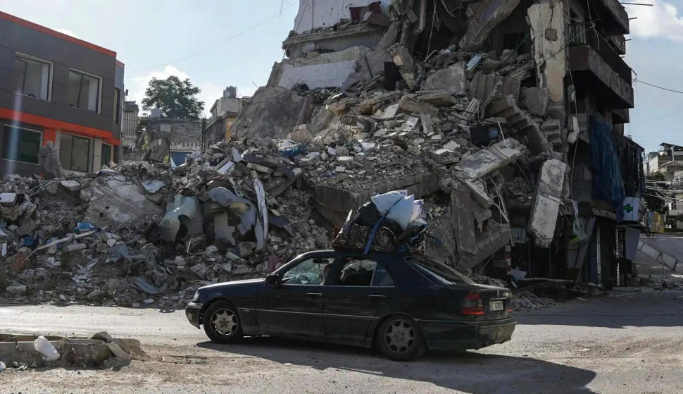 TOPSHOT - A car loaded with belongings drives past a destroyed building in Nabatieh on June 15, 2026. The United States and Iran said they reached a deal to end the Middle East war on all fronts including Lebanon, and reopen the vital Strait of Hormuz, but offered little indication on the thorny question of Tehran's nuclear programme. Washington and Islamabad said the agreement was to be signed on June 19 in Switzerland, signalling what would be a major breakthrough to ending months of war that have taken thousands of lives and roiled energy markets. (Photo by Abbas FAKIH/AFP)/ALTERNATIVE CROP