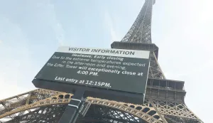 This photograph taken through a window shows the Eiffel Tower with a giant screen announcing its early closing due to heatwave in Paris on June 23, 2026. A deadly heatwave has battered France since last week, disrupting daily life as well as forcing school closures and train cancellations. "Due to the high temperatures forecast, the Eiffel Tower will be adjusting its operations," said the operator of the monument made of latticed steel girders. (Photo by Charlotte SIEMON/AFP)