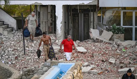 People carry their belongings out of a damaged building following an earthquake in Catia La Mar, La Guaira state, some 30km north-west of Caracas, on June 25, 2026. A twin earthquake that was Venezuela's largest in over a century has killed at least 164 people and destroyed multiple buildings near the capital, where residents searched on June 25 for missing relatives. (Photo by Federico PARRA/AFP)