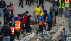 Rescuers and volunteers carry a person on a stretcher after being pulled alive from the rubble of a collapsed building in Caraballeda, La Guaira state, Venezuela, on June 28, 2026, following earthquakes. Thousands of rescuers, relatives and volunteers dig day and night through mounds of concrete to find survivors of the earthquakes that struck Venezuela more than three days ago, leaving nearly 1,500 dead and tens of thousands missing. (Photo by Miguel MEDINA/POOL/AFP)
