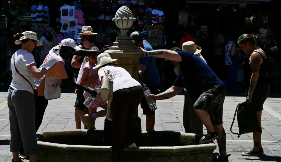 People fill bottles from a public water fountain during a heatwave in Venice on June 27, 2026. (Photo by Stefano RELLANDINI/AFP)