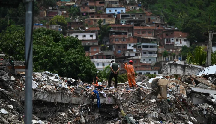 A rescue worker raises his hand to silence people to try to find survivors at a collapsed building following the June 24 twin earthquakes, in Caraballeda, La Guaira state, Venezuela, on June 30, 2026,. Tens of thousands of people urgently need food and shelter in Venezuela due to the devastation from two huge earthquakes that killed more than 1,700 and injured 5,000, the UN said on June 30, 2026, as doctors warned of potential outbreaks of disease. (Photo by Juan BARRETO/AFP)