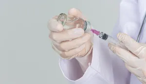 Young doctor is holding hypodermic syringe with vaccine vial rubber gloves on gray background.OSPICE CJEPIVO CIJEPLJENJE