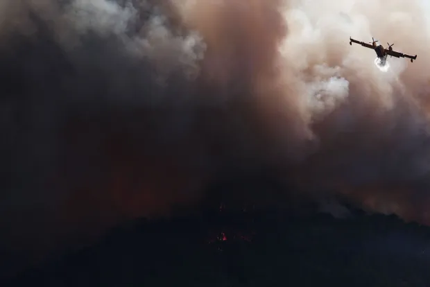 (FILES) A French Civil Security Canadair CL-415 aircraft sprays water on a forest surrounding Cotignac, southeastern France on July 23, 2026 during a wildfire. France has been battered by three heatwaves since May as part of increasingly common extreme weather episodes linked to climate change, causing thousands of excess deaths and fuelling wildfires. (Photo by Thibaud MORITZ/AFP)