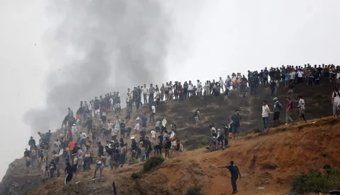 TOPSHOT - People gather on a hilltop as smoke billows from the site of clashes near Fnideq, on the Morocco-Spain border, on July 31, 2026. Thousands of migrants crossed overnight from Morocco into Spain's north Africa's Ceuta enclave, a police source said on July 31, adding that it was impossible to estimate how many people in total. A total of 18 people died while attempting to reach the Spanish enclave, the source said. (Photo by Abdel Majid BZIOUAT/AFP)