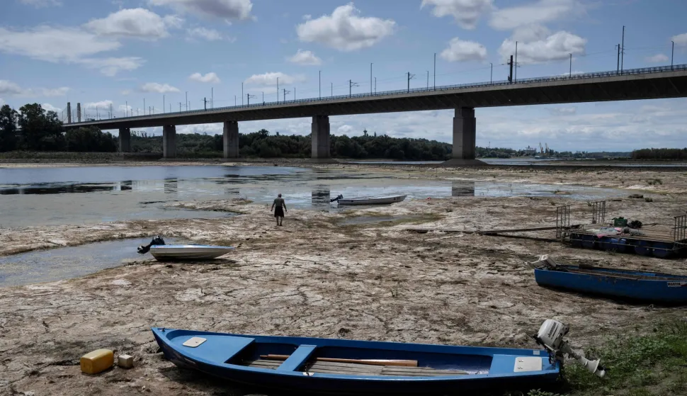 A fisherman tries to move his boat, blocked by algae on the bottom of the Danube river in front of the Calafat-Vidin bridge, connecting Bulgaria and Romania near the village Antimovo, southeastern Bulgaria, on July 22, 2026. At the Romanian town of Corabia on the banks of the Danube river, some boats are stranded in shallow water full of algae in the touristic port, which lies deserted as ships can no longer dock due to sandbars (Photo by Nikolay DOYCHINOV/AFP)