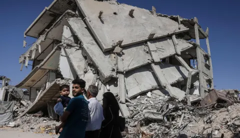 A Palestinian man carrying a child walks past a destroyed building in Khan Yunis in the southern Gaza Strip on July 31, 2026. Hamas said on July 31, 2026, it had agreed to a deal announced by the US president to end its war with Israel, which includes it handing over its weapons to a Palestinian governing committee and the gradual withdrawal of Israeli forces from Gaza. (Photo by Bashar Taleb/AFP)