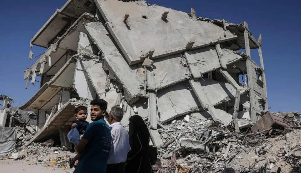 A Palestinian man carrying a child walks past a destroyed building in Khan Yunis in the southern Gaza Strip on July 31, 2026. Hamas said on July 31, 2026, it had agreed to a deal announced by the US president to end its war with Israel, which includes it handing over its weapons to a Palestinian governing committee and the gradual withdrawal of Israeli forces from Gaza. (Photo by Bashar Taleb/AFP)