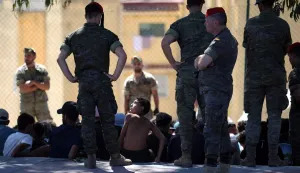 A young migrant (C) looks at a member of the Spanish Army's 'Regulares' infantry force who watches a group of migrants near the border post of the Spanish enclave of Ceuta on August 2, 2026. At least 72 people died during last week's mass influx of migrants into Spain's Ceuta enclave, when tens of thousands of people mostly swam around the border post from Morocco, local officials said today. Most of the estimated 60,000 people who rushed into Spain's north African territory have returned to Morocco since the territory's largest mass migrant crossing. (Photo by Henry NICHOLLS/AFP)