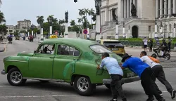 People push an old car along a street in Havana on July 29, 2026. Cuba began to liberalise certain sectors of its economy, drastically reducing the number of activities prohibited to private companies, a few weeks after the parliament approved a package of 176 measures in favour of the market economy. (Photo by YAMIL LAGE/AFP)