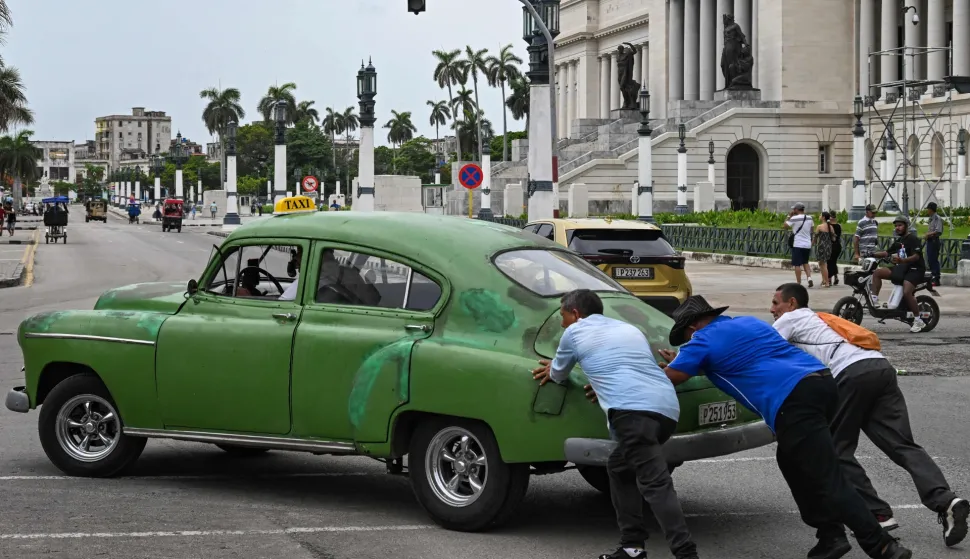 People push an old car along a street in Havana on July 29, 2026. Cuba began to liberalise certain sectors of its economy, drastically reducing the number of activities prohibited to private companies, a few weeks after the parliament approved a package of 176 measures in favour of the market economy. (Photo by YAMIL LAGE/AFP)