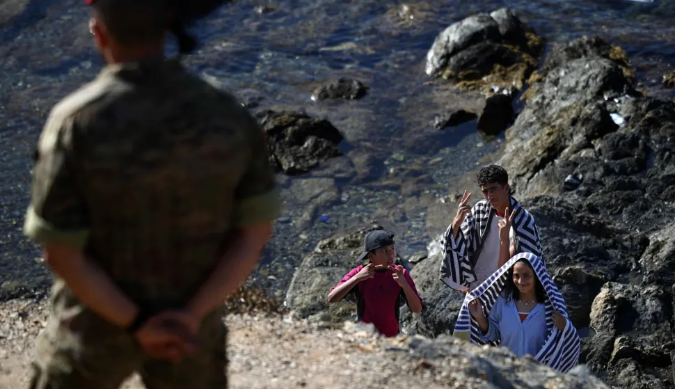 A member of the Spanish Army's 'Regulares' infantry forces watches a group of migrants near the border post of the Spanish enclave of Ceuta on August 2, 2026. At least 72 people died during last week's mass influx of migrants into Spain's Ceuta enclave, when tens of thousands of people mostly swam around the border post from Morocco, local officials said today. Most of the estimated 60,000 people who rushed into Spain's north African territory have returned to Morocco since the territory's largest mass migrant crossing. (Photo by Henry NICHOLLS/AFP)