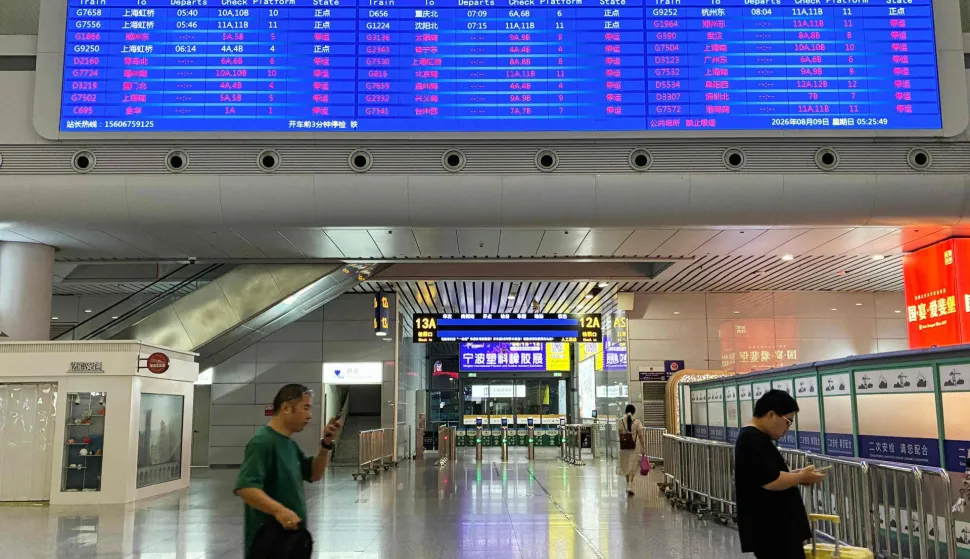 Passengers walk under a departure board at Ningbo railway station as most trains are cancelled due to approaching Typhoon Dolphin on August 9, 2026. (Photo by Rebecca BAILEY/AFP)