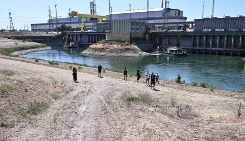 Journalists stand in front of Paks Nuclear Power Plant?s water intake structure and cold-water canal working with water from the river Danube in Paks on July 31, 2026. Amid prolonged heatwave conditions and air temperatures exceeding 35?C, the Danube has fallen to record low levels, creating a critical operational challenge for the plant. The extraordinary low-water situation has raised the prospect of a complete shutdown to ensure the continued safe cooling of the reactor units. (Photo by Attila KISBENEDEK/AFP)