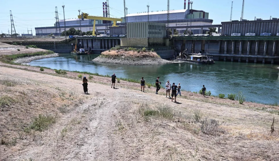Journalists stand in front of Paks Nuclear Power Plant?s water intake structure and cold-water canal working with water from the river Danube in Paks on July 31, 2026. Amid prolonged heatwave conditions and air temperatures exceeding 35?C, the Danube has fallen to record low levels, creating a critical operational challenge for the plant. The extraordinary low-water situation has raised the prospect of a complete shutdown to ensure the continued safe cooling of the reactor units. (Photo by Attila KISBENEDEK/AFP)
