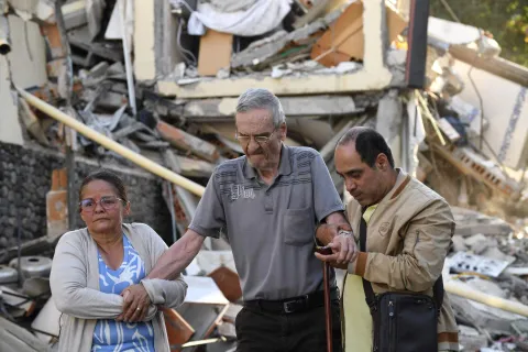 An elderly man receives help walking past the rubble of a collapsed building after an earthquake in Pereira, Colombia on August 10, 2026. A magnitude 7.4 earthquake struck Colombia on August 10, 2026, and killed at least 111 people, damaged more than 1,500 buildings, and left an unknown number of people buried under rubble. The government declared a state of emergency to attend to the quake that shook several cities across the coffee-producing region, the Pacific coast, and neighboring Latin American countries, sending terrified residents racing into the street. (Photo by Jaime SALDARRIAGA/AFP)
