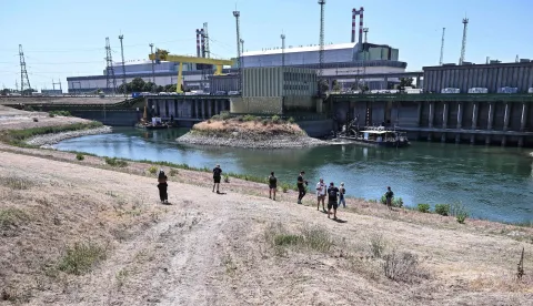 Journalists stand in front of Paks Nuclear Power Plant?s water intake structure and cold-water canal working with water from the river Danube in Paks on July 31, 2026. Amid prolonged heatwave conditions and air temperatures exceeding 35?C, the Danube has fallen to record low levels, creating a critical operational challenge for the plant. The extraordinary low-water situation has raised the prospect of a complete shutdown to ensure the continued safe cooling of the reactor units. (Photo by Attila KISBENEDEK/AFP)