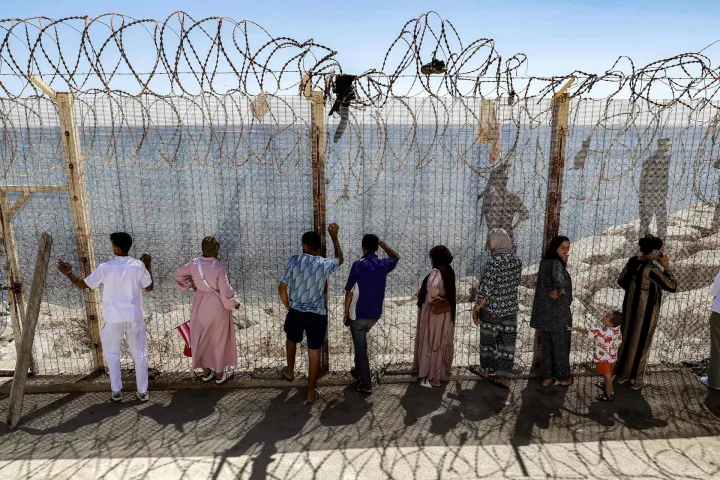 TOPSHOT - Relatives and friends wait by a fence topped with barbed-wire for the return of people who had previously crossed into Spain's North African enclave of Ceuta, at Morocca's Bab Sebta border crossing on the outskirts of Fnideq on August 2, 2026. As many as 60,000 migrants entered Ceuta in recent days, mostly swimming around the small border post that juts into the Mediterranean Sea, in an unprecedented surge that prompted an international crisis for Spain. The mass crossing into the tiny Spanish territory resulted in at least 67 deaths, according to Spanish authorities, and led to clashes with Moroccan police on the shared border. (Photo by Abdel Majid BZIOUAT/AFP)