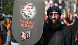 A man holds a placard depicting US President Donald Trump and displaying the words "There Will Be Blood" as they gather at Ferdowsi Square for the funeral procession of Iran's slain Supreme Leader Ali Khamenei in Tehran July 6, 2026. Massive crowds are expected on July 6 for the funeral procession of late Iranian supreme leader Ali Khamenei in Tehran, with authorities hoping to avoid a repeat of the chaos that accompanied his predecessor's funeral. (Photo by Wakil Kohsar/AFP)/