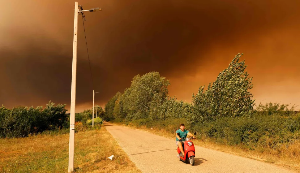 TOPSHOT - A man rides a scooter beneath a smoke-filled sky as a wildfire burns in Deliblatska Pescara (Deliblato Sands), near the village of Grebenac, some 70 kilometres northeast of Belgrade, Serbia, on August 20, 2026. Firefighters were battling wildfires across the Balkans as days of high temperatures and drought conditions continue to drive blazes in several countries, including Serbia. Scientists have long warned that climate change caused by human use of fossil fuels will make periods of drought more intense and longer-lasting, creating the ideal conditions for wildfires. (Photo by Uros Arsic/AFP)