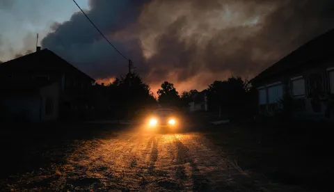 A car drives through the village of Grebenac as thick smoke from a wildfire engulfs the sky over Deliblatska Pescara (Deliblato Sands), some 70 kilometres northeast of Belgrade on August 20, 2026. Firefighters were battling wildfires across the Balkans as days of high temperatures and drought conditions continue to drive blazes in several countries, including Serbia. Scientists have long warned that climate change caused by human use of fossil fuels will make periods of drought more intense and longer-lasting, creating the ideal conditions for wildfires. (Photo by Uros Arsic/AFP)