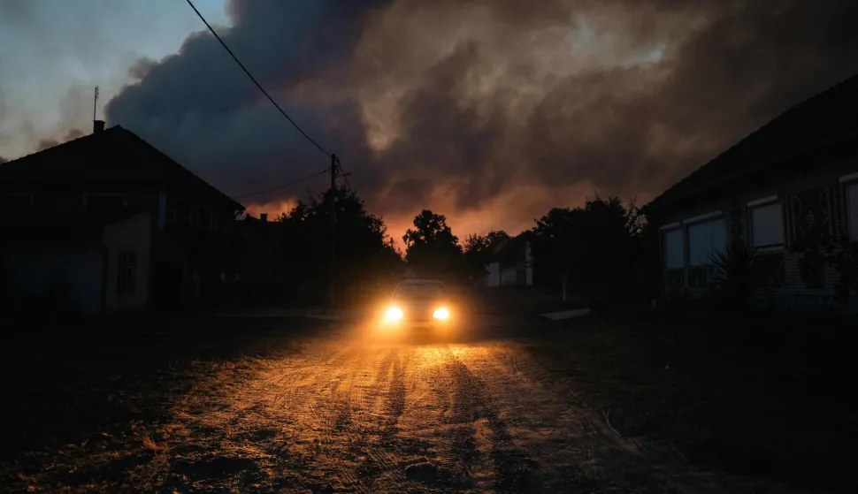 A car drives through the village of Grebenac as thick smoke from a wildfire engulfs the sky over Deliblatska Pescara (Deliblato Sands), some 70 kilometres northeast of Belgrade on August 20, 2026. Firefighters were battling wildfires across the Balkans as days of high temperatures and drought conditions continue to drive blazes in several countries, including Serbia. Scientists have long warned that climate change caused by human use of fossil fuels will make periods of drought more intense and longer-lasting, creating the ideal conditions for wildfires. (Photo by Uros Arsic/AFP)