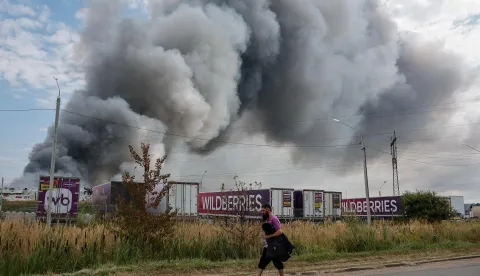 A Wildberries emloyee walks past a plume of smoke rises during a fire at Russian e-commerce firm Wildberries' logistics complex near the town of Podolsk, outside Moscow on August 16, 2026. Hundreds of drones targeted Moscow on August 16, 2026 as Russia launched missile strikes that killed three people and wounded more than a dozen in Kyiv and other Ukrainian cities, officials on the two sides said. Ukraine has increasingly targeted warehouses linked to the Wildberries online retailer, arguing its strikes are a response to Moscow's bombardment of Ukrainian towns and infrastructure. (Photo by TATYANA MAKEYEVA/AFP)