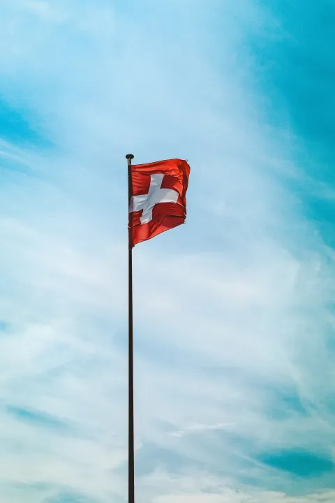 A low angle shot of Switzerland flag on a pole under the breathtaking cloudy sky