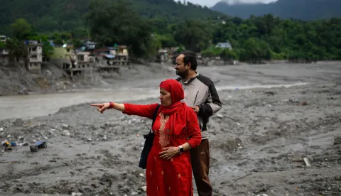 A woman points at damaged houses across the Trishuli river in the aftermath of flash floods at Devighat in Nepal's Nuwakot district on August 29, 2026. Nearly 3,000 people were still missing on August 29 and 633 confirmed dead after flash floods and landslides hit the Nepal-Tibet border. (Photo by MANAN VATSYAYANA/AFP)