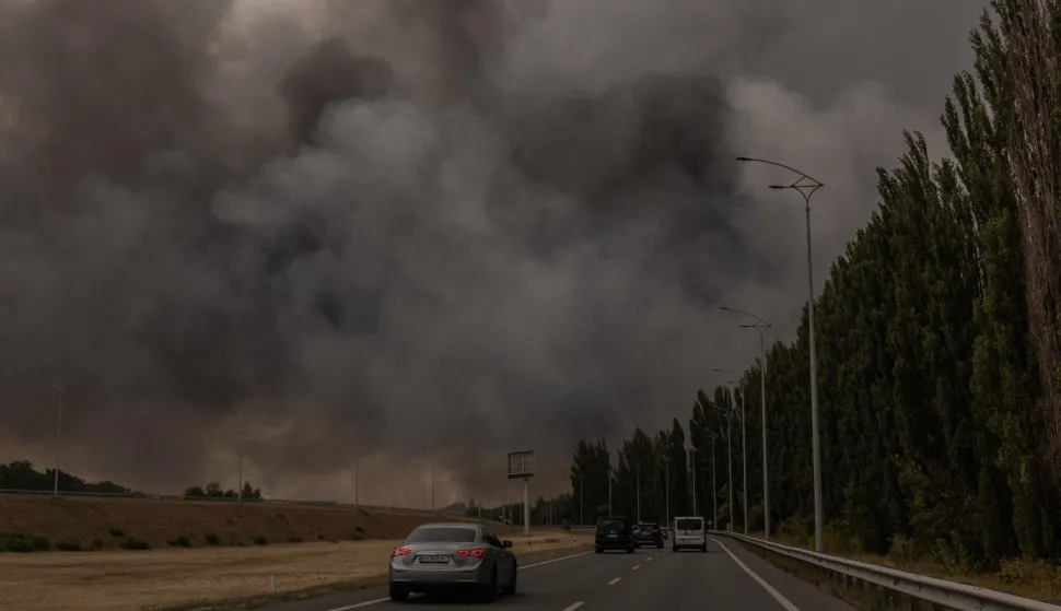 Cars drive on a road as smoke rises in the distance from a warehouse following a Russian air attack near Boryspil, Kyiv region on August 27, 2026, amid the Russian invasion of Ukraine. (Photo by Roman PILIPEY/AFP)
