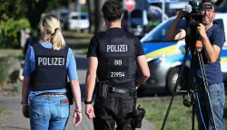 Police officers walk near the scene at a school in Gosen-Neu Zittau, south-east of Berlin on August 27, 2026, after two people were killed in a "violent incident" at the school. Local media reported August 27 that an 18-year-old female student and a 30-year-old man had died. Regional public broadcaster RBB and a local daily said that an alarm had been triggered at a secondary school in the town of Gosen-Neu Zittau, with police confirming they were on the scene and that a suspect had been arrested. (Photo by RALF HIRSCHBERGER/AFP)