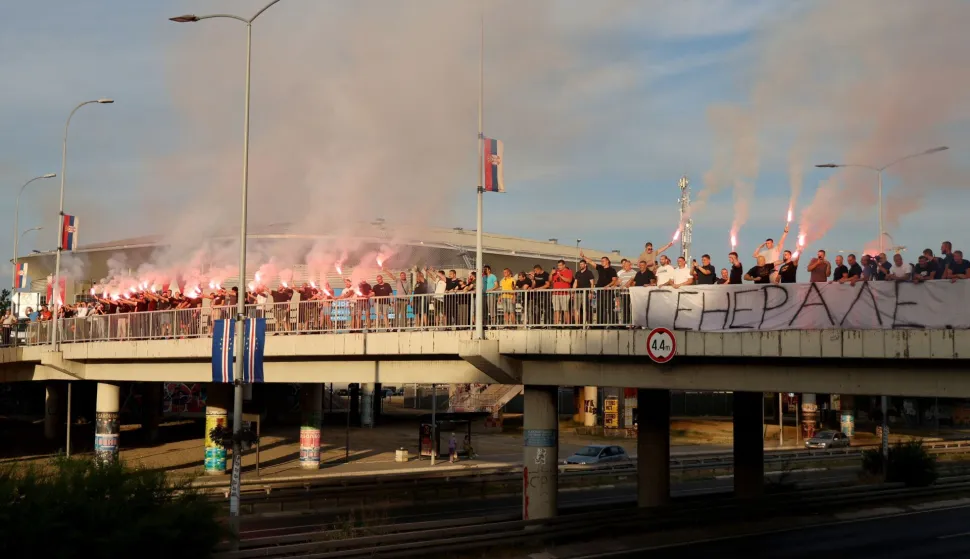 A group of people gathered on a footbridge over a motorway light flares while holding a banner reading "General" as they greet a convoy carrying the body of Bosnian Serb war criminal Ratko Mladic as it passes through Belgrade, Serbia, on September 3, 2026. Mladic's body arrived in Serbia earlier in the day and was driven from the airport under police escort after being received with military honours. Mladic died the previous week while serving a life sentence for genocide, war crimes and crimes against humanity committed during the 1992-1995 Bosnian war. (Photo by Pedja MILOSAVLJEVIC/AFP)