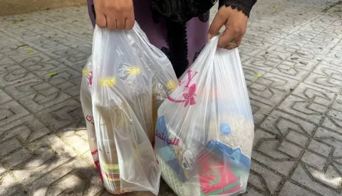 A woman carries plastic bags filled with cooking oil, sugar, pasta, and other rations she bought using her government-subsidised family ration-card, in Cairo on August 17, 2026. Egypt removed 850,000 people from its subsidy system since June, according to the supply ministry, as part of reforms that will reportedly exclude millions more in 2027. The measures aim to cut the cost of one of the world's largest food subsidy programmes, as Egypt pursues International Monetary Fund-backed reforms. (Photo by Khaled DESOUKI/AFP)