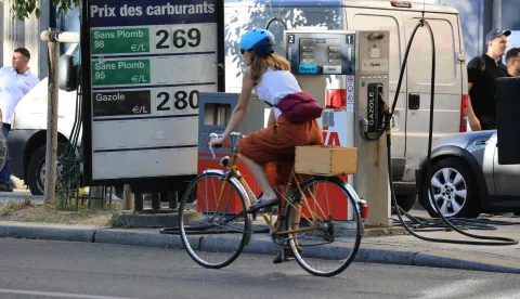 A cyclist rides her bicycle past a board indicating fuel prices at a petrol station in Paris on September 14, 2026. (Photo by Ludovic MARIN/AFP)