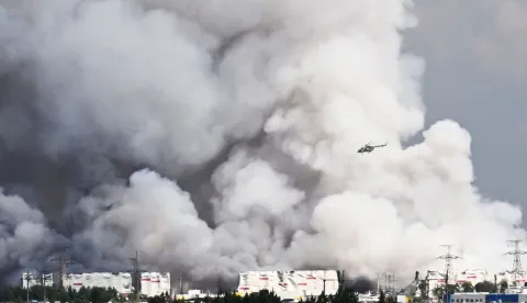 A helicopter flies past smoke rising from a warehouse for a Russian e-commerce giant near Saint Petersburg after being hit by Ukrainian drones early on July 24, 2026 morning, triggering a fire that sent smoke pouring over the historic city, according to local officials. At least 17 people were killed on July 24, 2026 in Russian and Ukrainian long-range strikes -- including just outside Kyiv and hundreds of miles east of Moscow -- as both sides intensify strikes with diplomacy in a deadlock. Ukraine also attacked warehouses belonging to Russian online retail giant Wildberries outside Saint Petersburg -- targeting Russia's equivalent of Amazon for the third time this week. (Photo by AFP)