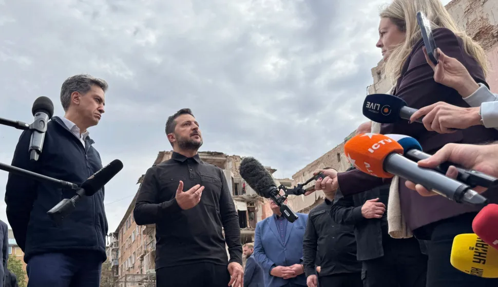 Ukraine's President Volodymyr Zelensky (C) and Britain's Foreign Secretary Ed Miliband (L) speak to the press outside a multi-storey residential building in Pryluky, on October 8, 2026, the day following its destruction during a Russian aerial attack, amid the Russian invasion of Ukraine. (Photo by Sergii VOLSKYI/AFP)