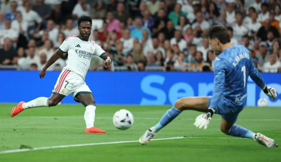 Real Madrid's Brazilian forward #07 Vinicius Junior (L) shoots challenged by Real Sociedad's Spanish goalkeeper #01 Alex Remiro during the Spanish league football match between Real Madrid CF and Real Sociedad at Santiago Bernabeu Stadium in Madrid on August 26, 2026. (Photo by Thomas COEX/AFP)