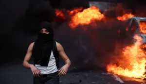 TOPSHOT - A protester walks past a car on fire during a demonstration to protest against the "high cost of living", in Paris on October 17, 2026 as part of a nationwide call for mobilisation bringing together various groups expressing their anger: former "Yellow Vests", secondary school and university students, climate activists and even farmers. After weeks of student protests, France faces broader, nationwide demonstrations on October 17, 2026 over the cost of living, setting up a potentially fraught six months heading into a presidential election. A police source told AFP that authorities estimated nearly 200,000 people could take part, with 40,000 in Paris. (Photo by Kiran RIDLEY/AFP)