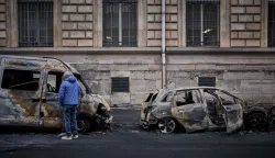 A local resident looks inside a burnt out van on Rue Yves Toudic destroyed after a weekend of protests against the "high cost of living", in central Paris on October 19, 2026. France's Prime Minister said 1,200 people were arrested in protests across the country on October 17, and 150 police were hurt during clashes between police and protesters. Massive looting and multiple blazes gripped France as nationwide marches against soaring inflation degenerated into street violence of "extreme intensity". (Photo by Kiran RIDLEY/AFP)